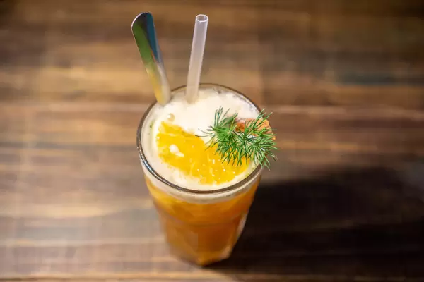 Orangen-Zimt Tee mit Eiswürfeln, Orangenscheibe und Rosmarin in Cocktailglas mit Löffel und Strohhalm