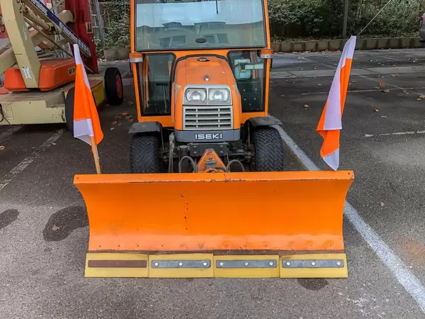 Oranges Fahrzeug von Iseki für Schneeräumung im Winter mit in Front montierter Schaufel und Flaggen