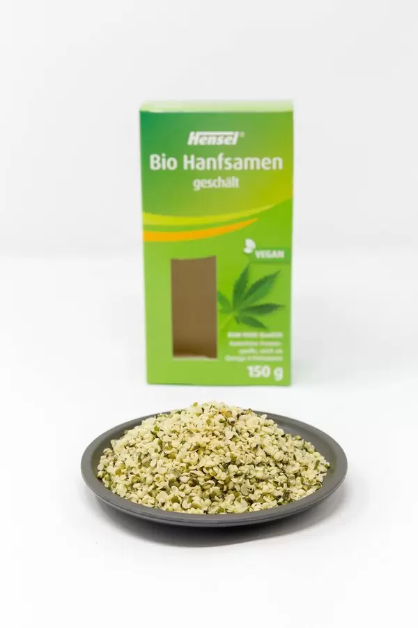 Organic vegan peeled hemp seeds on a plate in front of the packaging on white Background