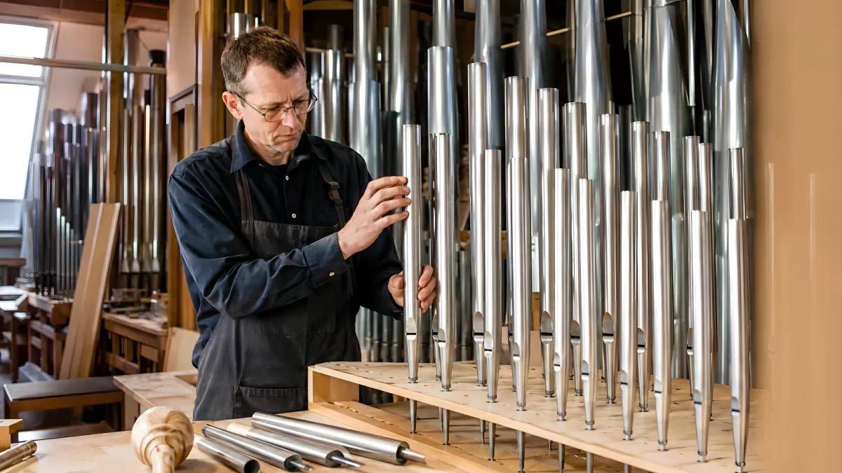 Orgelbauer justiert Metallpfeifen in der Werkstatt