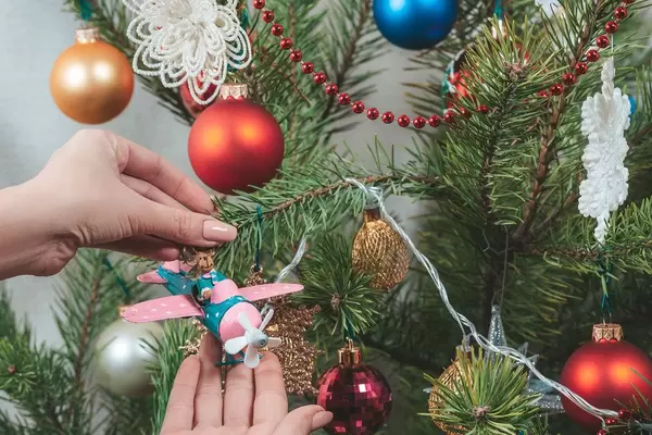 Ornamente für den Adventsbaum: Mädchen hängt einen Hirsch im Flugzeug an den geschmückten Weihnachtsbaum