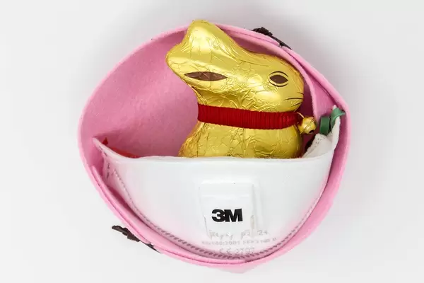 Ostern feiern in Corona-Zeiten: Lindt Goldhase und FFP3 Atemschutzmaske von 3M in Ostern-Deko vor weißem Hintergrund