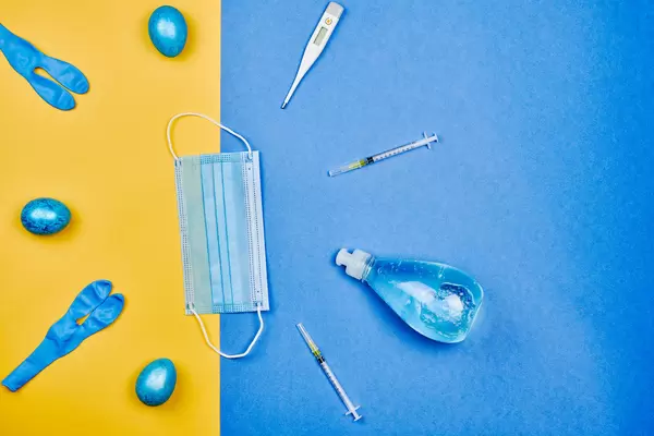 Ostern und Covid-19: gefärbte Eier, Thermometer, Spritzen, Mundschutz und Desinfektionsmittel