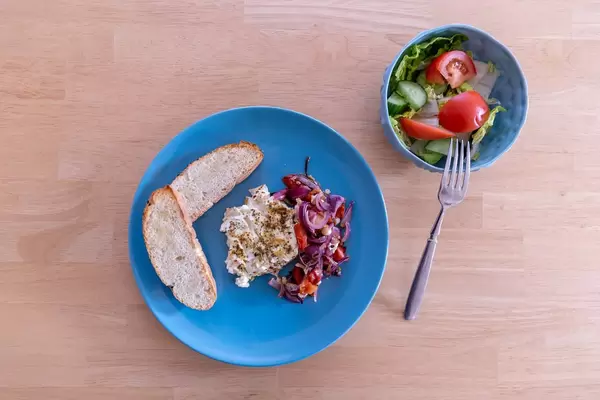 Oven-baked shepherd feta cheese with tomatoes, red onions and garlic bread on a blue plate with a fresh mixed salad in a bowl