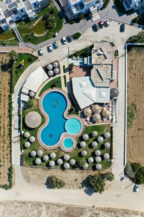 Overhead aerial shot of villa with large swimming pool and round parasols in Naxos, Cyclades, Greece