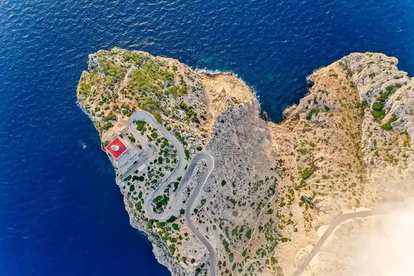 Overhead drone shot: the steep cliffs, rugged landscape and lighthouse of Cap de Formentor