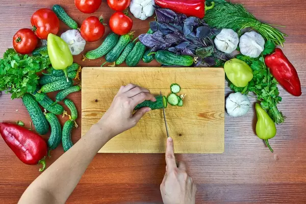 Overhead view of a woman slicing raw cucumber on cutting board