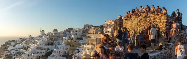 Overtourism in Santorini: panoramic shot of crowds gathering to watch and photograph the sunset