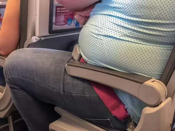 Overweight Passenger on the airplane, sitting constricted on the seat with no space