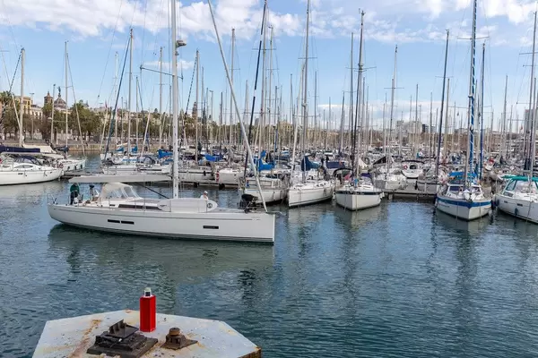 Paar fährt mit Segelboot in den Hafen Port Vell an der Promenade Rambla de Mar ein, in Barcelona (Spanien)