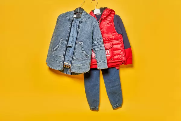 Pair of fashionable kid clothes hanged over the yellow backdrop