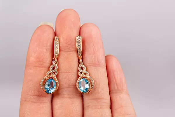 Pair of gold earrings with blue topaz in a female hand