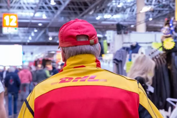 Paketbote des Kurierdienstes DHL in typisch gelb-roter Bekleidung von hinten