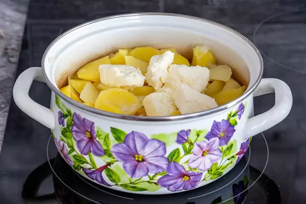 Pan with potatoes and pieces of butter on black kitchen cooking surface