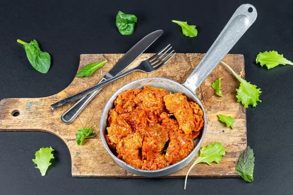 Pan with stewed fish in tomato sauce on a dark background with lettuce leaves (Flip 2020)