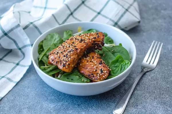 Panierter Teriyaki-Fisch mit Sesamöl auf Spinatblätter