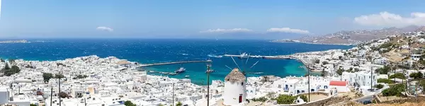 Panoramabild der Hauptstadt Mykonos mit weißen Häusern, einer Windmühle und blauem Meer
