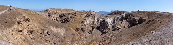 Panoramic photo of the volcanic landscape on Santorini: tourists taking a walk around the crater
