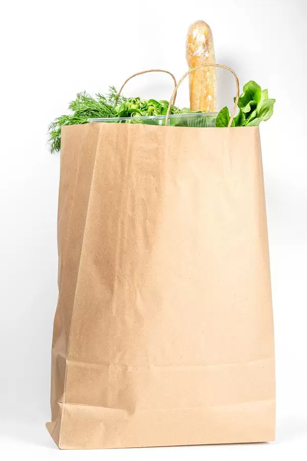 Paper bag with fresh herbs and baguette on a white background. Food purchasing concept
