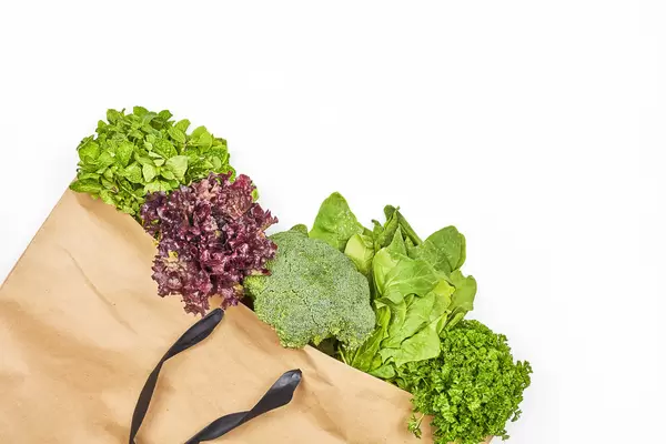 Paper bag with green leafy vegetables salad on white background
