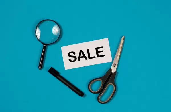 Paper with word Sale and scissors on blue background