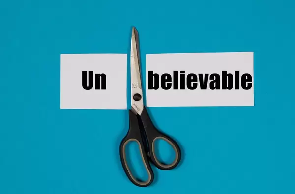 Paper with word Unbelievable and scissors on blue background