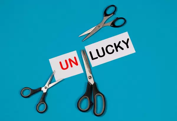 Paper with word Unlucky and scissors on blue background