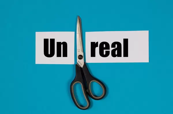 Paper with word Unreal and scissors on blue background