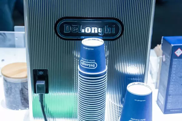 Pappbecher auf der Rückseite des DeLonghi Kaffeevollautomaten, neben ganzen Kaffeebohnen