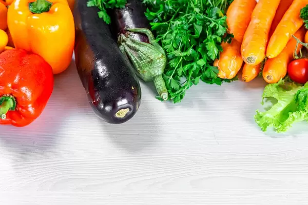 Paprika, dunkle Auberginen, Kräuter und Karotten, auf einem weißen Holztisch