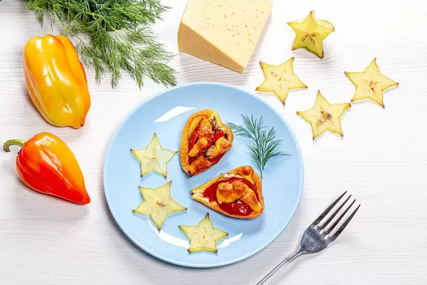 Paprikahälften gebacken und mit Tomaten und Käse gefüllt, auf blauem Teller, mit Scheiben aus frischer Karambole und Dill