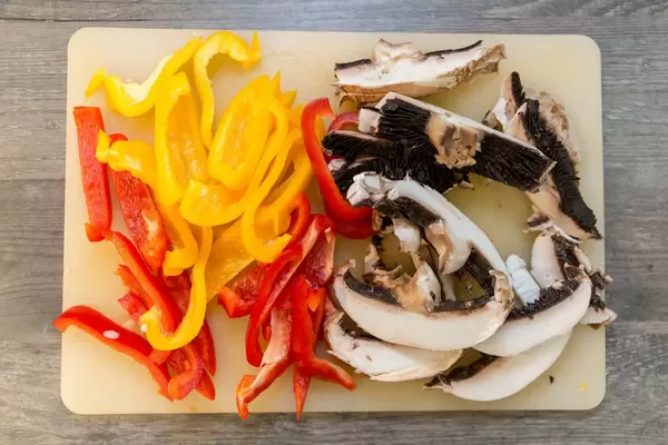 Paprikastreifen in rot und geld zusammen mit Pilzen auf einem Brettchen in der Aufsicht