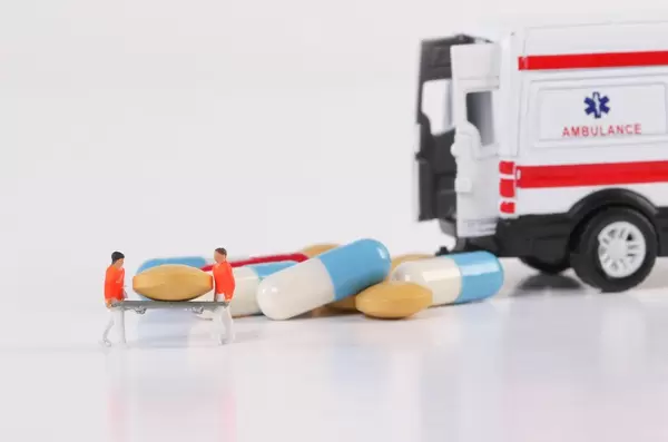 Paramedics with pills and ambulance car on white background