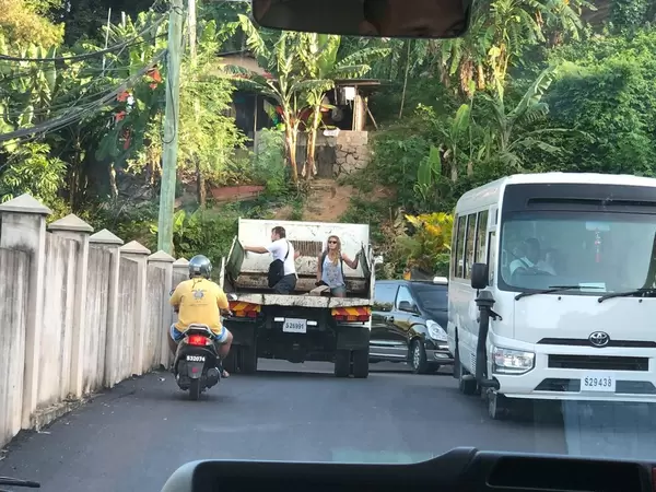 Pärchen fährt auf der Ladefläche eines Transporter mit, durch den Straßenverkehr in Baie Ste Anne auf Praslin, Seychellen