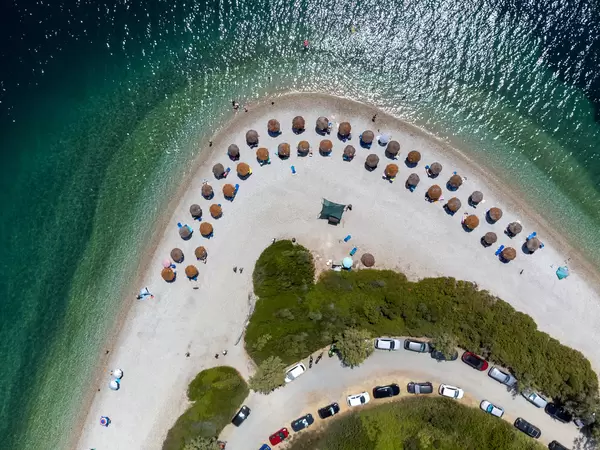 Parkplätze und Strohsonnenschirme am Kieselstrand von Agios Dimitrios (Alonnisos). Drohnenaufnahme