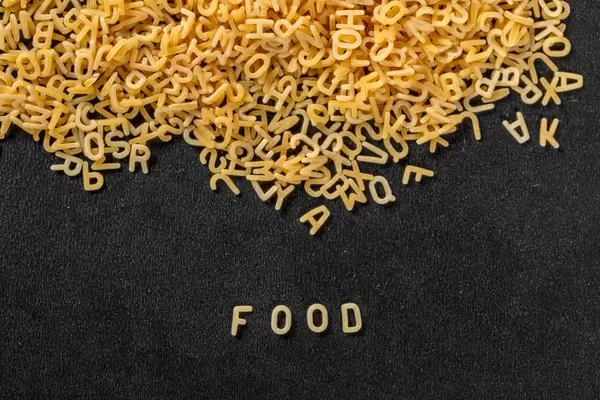 Pasta bildet das Wort Food aus zu Buchstaben geformten Nudeln vor schwarzem Hintergrund