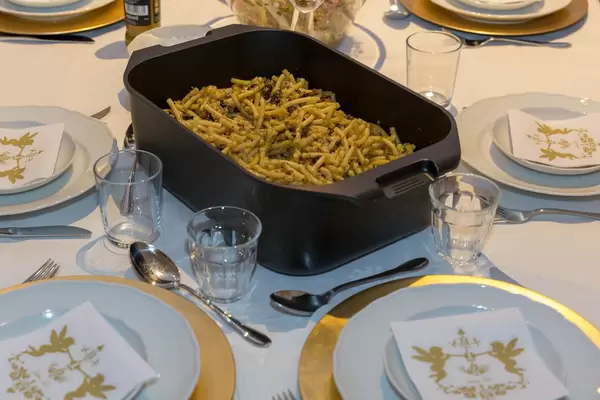 Pasta mit grüner Pestosoße und Kräutern in schwarzem Topf auf festlich gedecktem Tisch