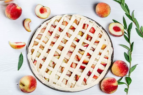 Peach pies and ingredients on white wooden background