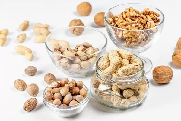 Peanuts, walnuts, pistachios and hazelnuts in glass bowls and in a jar on a white background (Flip 2020)