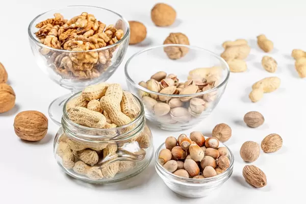Peanuts, walnuts, pistachios and hazelnuts in glass bowls and in a jar on a white background