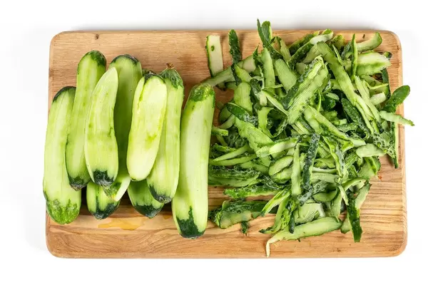 Peeled cucumbers and their green peel on wooden kitchen board