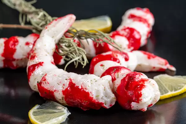Peeled prawns on a black plate with lemon slices
