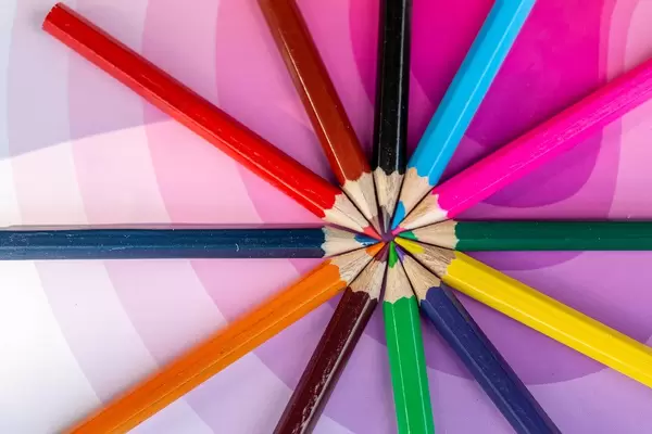 Pencils of different colors laid out on a pink background