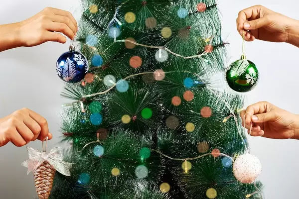 People holding Christmas decorations and baubles around the Xmas tree