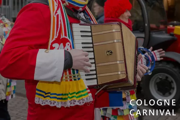 People in carnival costumes play the accordion during the carnival procession, next to the picture title "Cologne Carnival"