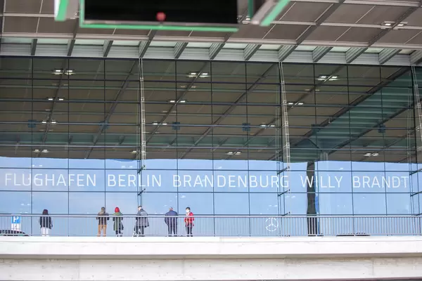 People in front of glass wall with writing "Flughafen Berlin Brandenburg Willy Brandt" at BER Terminal 1