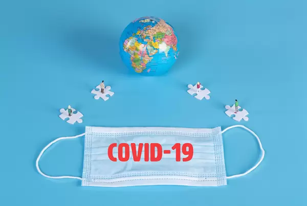 People standing on puzzle pieces, globe and medical face mask with Covid-19 text