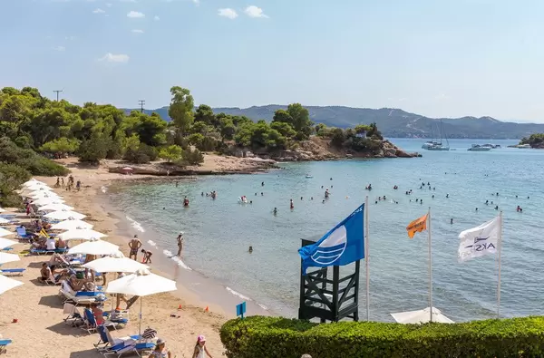 People swimming in the Myrtoan Sea, at a beach of the Aks Hinitsa Bay Hotel in Chinitsa, with beach chairs and white parasols