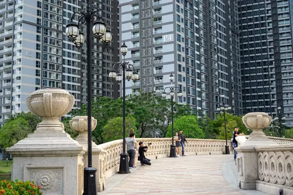 People taking Pictures on a Pedestrian Bridge at Vinhomes Central Park Attraction with Apartment Buildings in the Background in Saigon, Vietnam