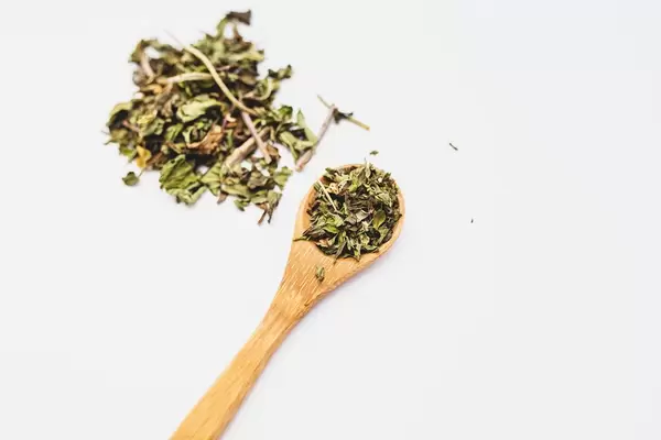 Peppemint loose leaf tea on a wooden spoon on white background